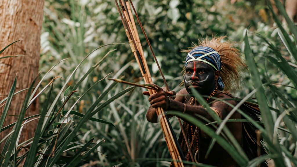 Tribal warrior with body paint and bow in Jayapura's lush jungle.